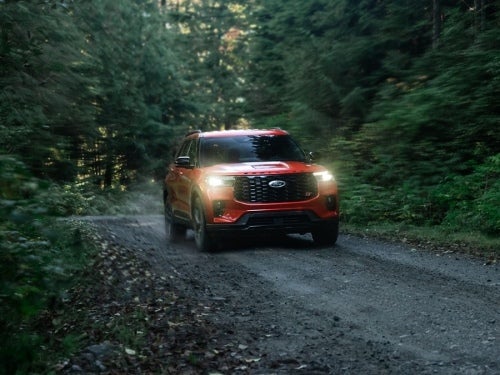 2025 Ford Explorer offroading on a rocky road between trees on a cloudy day with headlights on